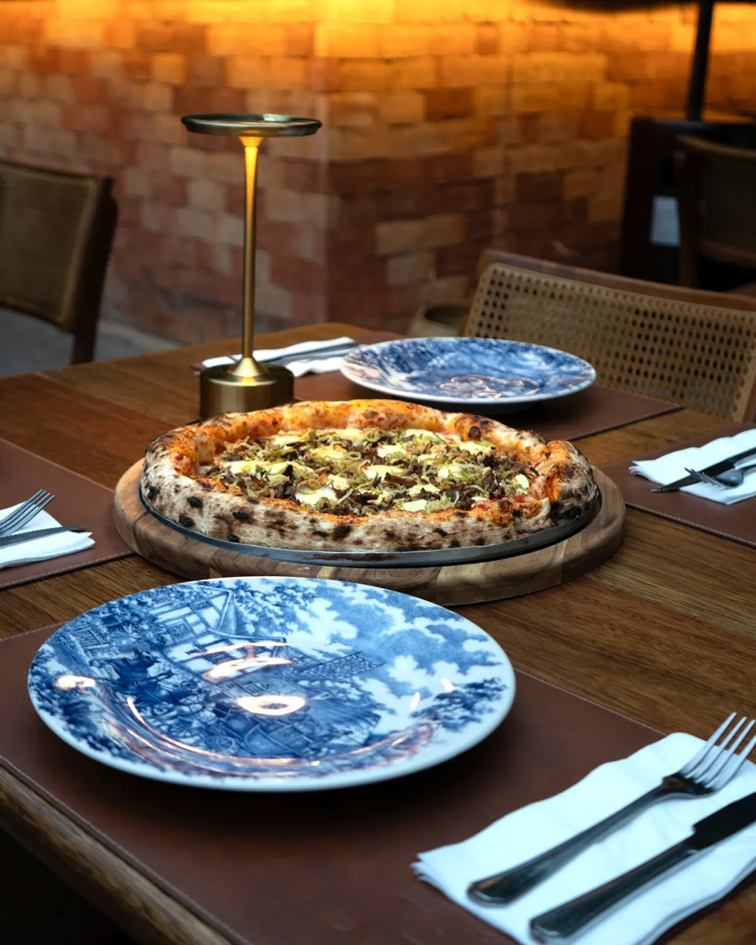 Pizza napolitana servida em tábua de madeira, mesa posta sob luz quente